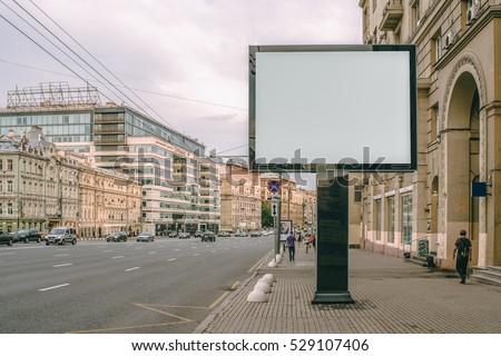 Horizontal blank billboard on the city street. In background buildings and road with cars. Mock up. The poster on the street next to the roadway.