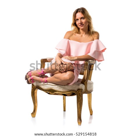 Pretty model woman posing in studio with a pink dress on vintage armchair