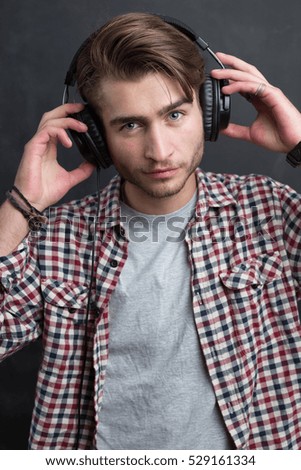 Portrait of confident young DJ with stylish haircut and headphones  on dark background.