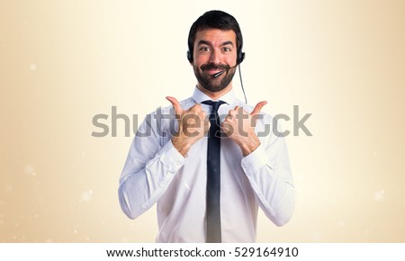 Young man with a headset with thumb up on ocher background