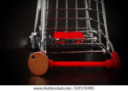 Shopping cart put beside the old and dirty fake one pound coin represent the retail business and supermarket background concept related idea.