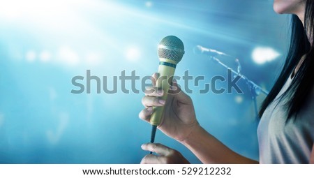 Woman holding microphone and singing on concert stage background