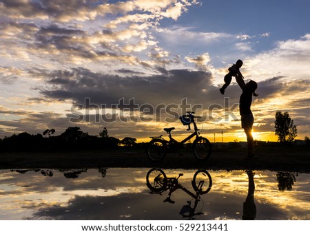 Reflection Silhouette of mother with her toddler against the sunset and bicycle. Asian family activity lifestyle.