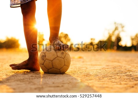 Close up picture of an old ball and foot of a kid who is playing football in the sunshine day.
