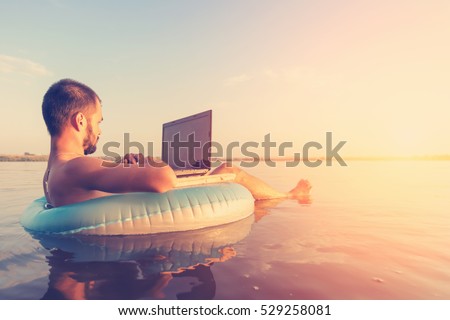 Man with a laptop on inflatable ring in the water Royalty-Free Stock Photo #529258081