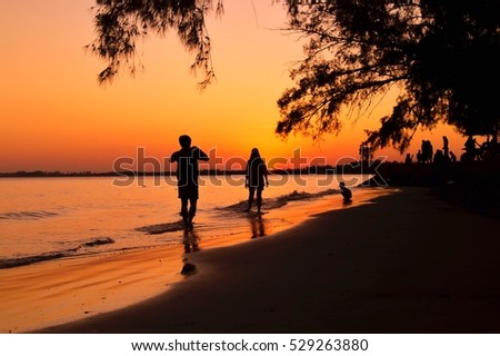 Silhouette of man taking picture his girlfriend on the beach at sunset
