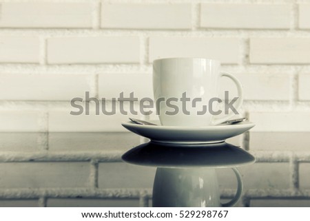 white cup of hot coffee on top of glass table with white brick wall background. concept fot drink and food