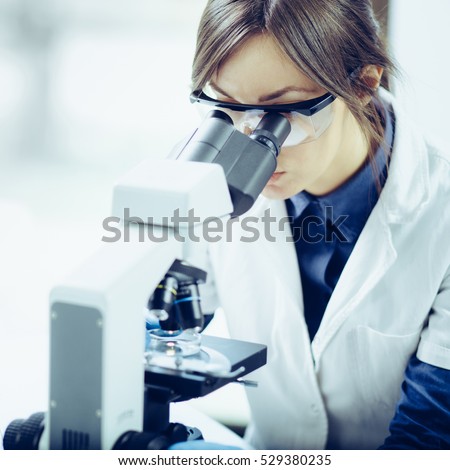 Young scientist looking through a microscope in a laboratory. Young scientist doing some research. Royalty-Free Stock Photo #529380235