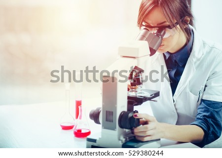Young scientist looking through a microscope in a laboratory. Young scientist doing some research. Royalty-Free Stock Photo #529380244
