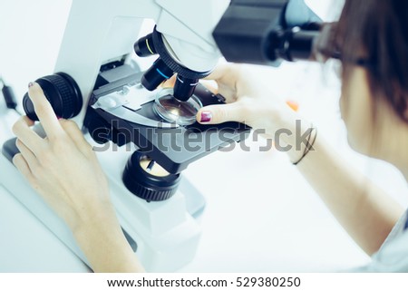Young scientist looking through a microscope in a laboratory. Young scientist doing some research. Royalty-Free Stock Photo #529380250