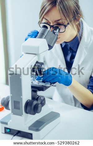 Young scientist looking through a microscope in a laboratory. Young scientist doing some research. Royalty-Free Stock Photo #529380262