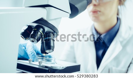 Young scientist looking through a microscope in a laboratory. Young scientist doing some research. Royalty-Free Stock Photo #529380283