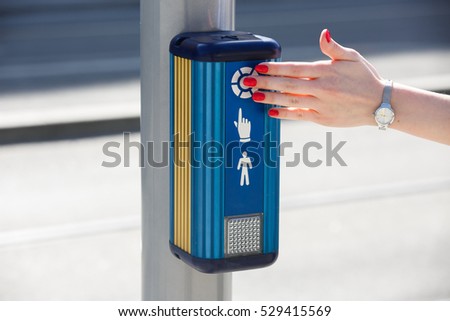 Delicate lady's hand pushes the button to turn on the traffic lights