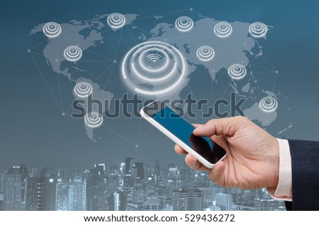 Businessman using blue screen mobile smartphone and city night in blue tone background with digital alarm wifi icon, internet of things IOT, smart city concept