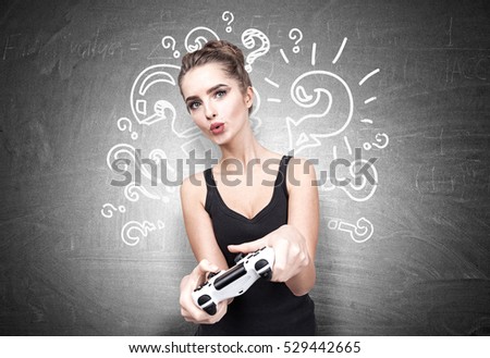 Geeky teenager girl is holding a video game controller and standing near a blackboard with question marks