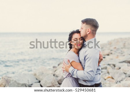 Bride in a purple dress  and groom  on the beach standing on rocks. Close-up. Royalty-Free Stock Photo #529450681
