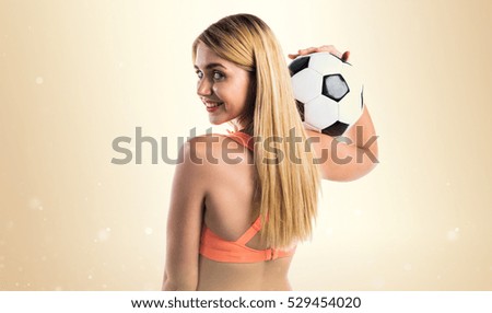 Pretty blonde girl holding a soccer ball on ocher background