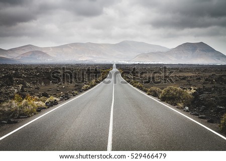 Endless road to Timanfaya National park in Lanzarote, Canary Ispands, Spain, Europe, Africa. Volcanic, black sand, harsh, tough, inhospitable, dry, sub-tropical, desert landscape. Royalty-Free Stock Photo #529466479