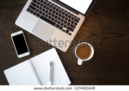 top view of laptop computer, smart phone, a cup of coffee, empty notebook on a wooden table
