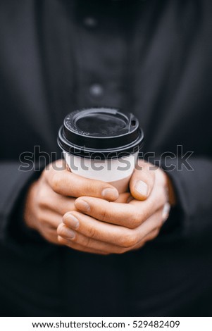 The guy holds a coffee Cup in hand on the street
