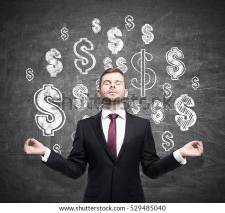 Portrait of a meditating businessman wearing a suit and a red tie and standing near a chalkboard with dollar signs depicted on it.