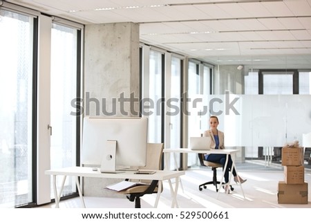 Computer monitor on desk with businesswoman working in background at office