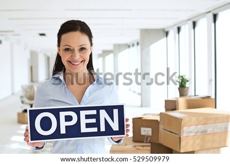 Portrait of smiling mid adult businesswoman holding open sign in new office