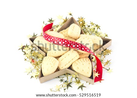 Christmas shortbread cookies in a star shaped box isolated against a white background and decorated with a gold wreathe and red spotted ribbon.