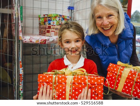 Little girl and her grandmother are posing for the camera with the charity Christmas box they have made. 