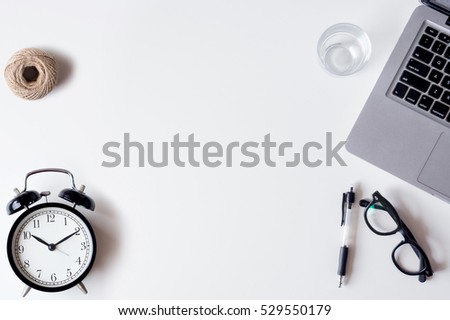 White office desk table with laptop, alarm clock, pen, rope, and glass. Top view with copy space, flat lay.