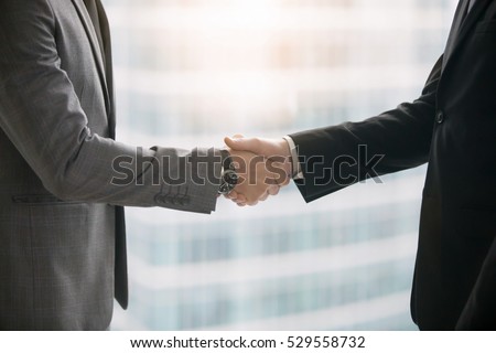 Close up of hands of two business partners making agreement, taking a big deal and shaking hands in meeting room at office. Urban style glass office building in big city on the background. Side view Royalty-Free Stock Photo #529558732