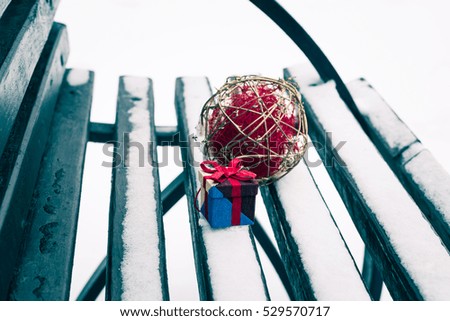 Small colorful gift box on a bench covered with snow