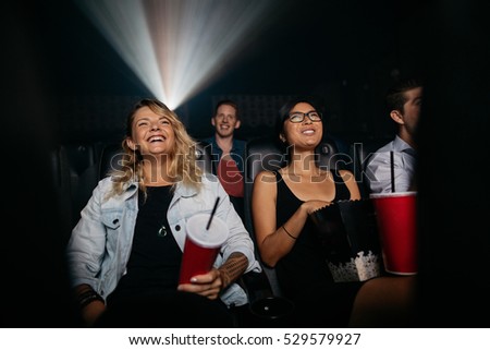 Young women and men watching movie in cinema. Group of people in theater with popcorn and drinks.