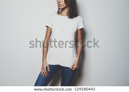 Young hipster girl wearing blue jeans and blank white t-shirt with empty area for your logo or design, mock-up of white cotton t-shirt, white wall in the background