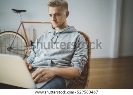 Young hipster man sitting at modern office or co-working space and using laptop, vintage bike in the background, male freelancer working from home, finance and technology concept