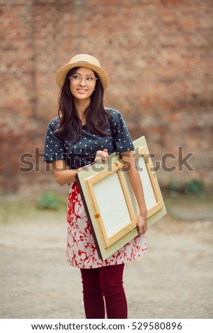 Young Asian woman with painting outdoors. Mixed race student girl on university college campus park smiling happy and looking at camera.