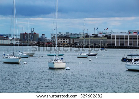 Sailboats moored in Boston harbor with the cityscape in the background and a storm building in the distance.