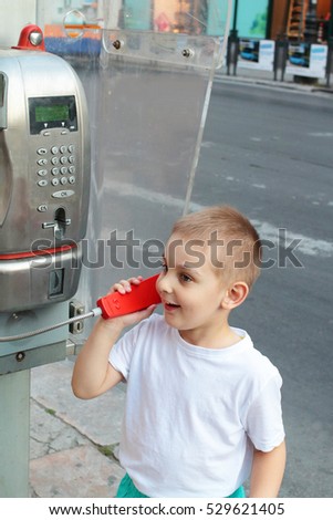 Cute blonde little boy is calling home using the public payphone