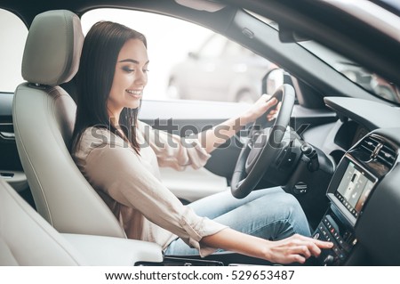 Searching for favorite music. Young attractive woman smiling and pushing buttons while driving a car Royalty-Free Stock Photo #529653487