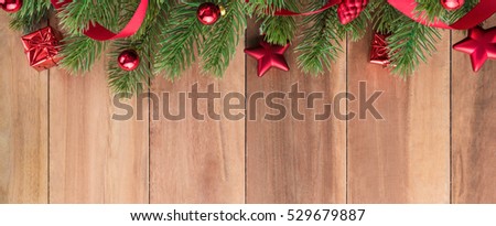 Green Christmas tree leaves with shiny red ornaments on wood background, border design banner