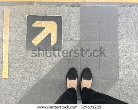 Woman with black pants and shoes standing at arrow entrance sign; waiting line