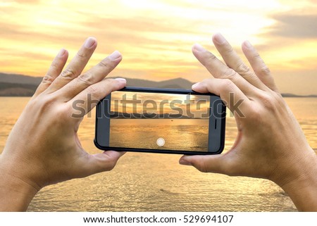 Two hands holding smart phone taking a photograph of sunset at Koh Samui, Thailand