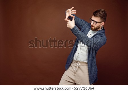 Young casual man putting hands in gesture of camera and pretending to make picture on brown background.