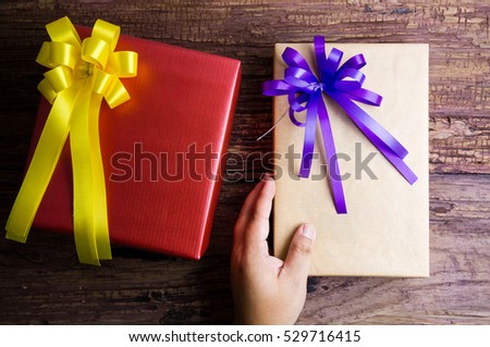 Hand and present gift box design wrapped in color paper with bows on a wooden background.View from above with copy space.Christmas and New Year background,