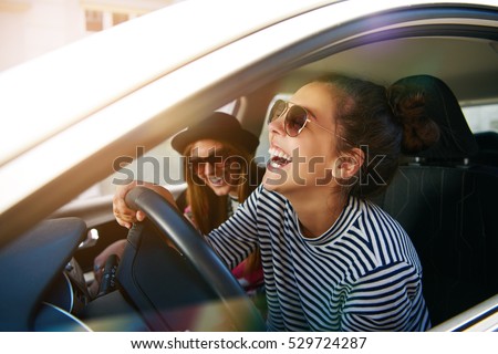 Laughing young woman wearing sunglasses driving a car with her girl friend , close up profile view through the open window Royalty-Free Stock Photo #529724287