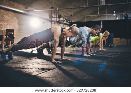 Group of adults doing push up exercises at indoor physical fitness cross-training exercise facility with bright light flare over them Royalty-Free Stock Photo #529728238