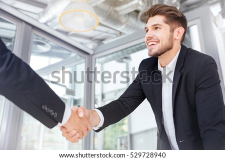 Two smiling successful young businessmen shaking hands on business meeting in office Royalty-Free Stock Photo #529728940