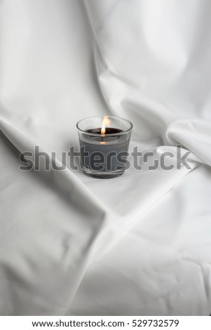 Flame light. Christmas candle burning at night. Abstract background. Silver light of candle flame. White silk background. Candle flame. Black candle against white silver background. Memorial. Meditate