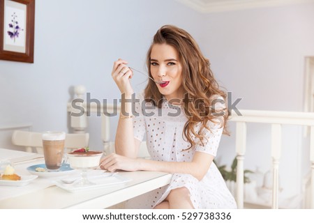Attractive happy young woman sitting and eating dessert in cafe