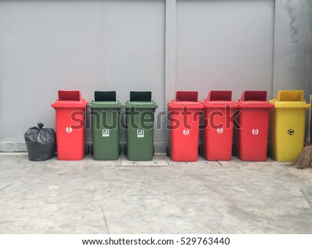 Wheel recycle bins in red, yellow and green for waste separation with black bin bag and wall background